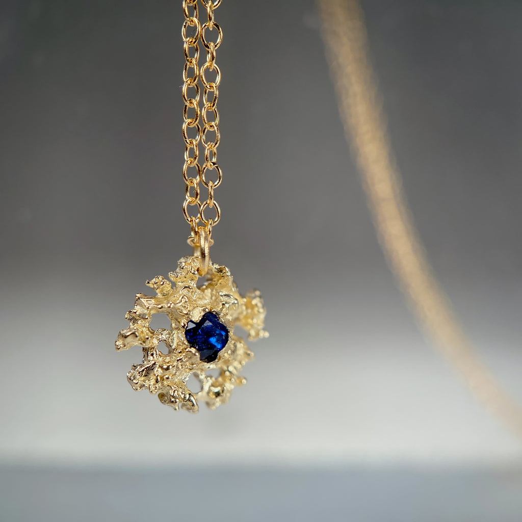 Lacy, textured, star-like pendant has center stone; shown here with a blue sapphire