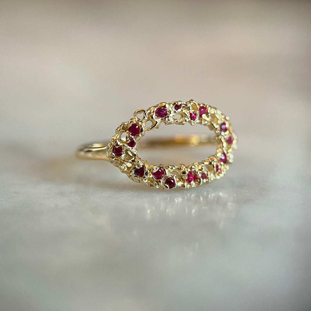 A light and airy open oval gold ring; lacy with organic holes; shown with scattered tiny rubies of various sizes